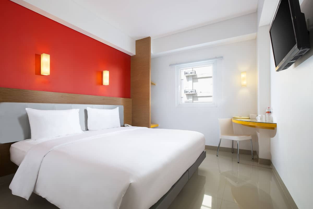 Habitació d'hotel amb un llit gran, un escriptori, una cadira, un televisor i una finestra.