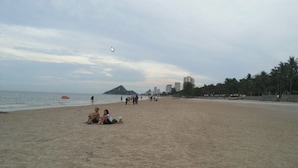 A beach with people sitting and walking, a boat in the water, and buildings in the background. - Baan Suksabai Hua Hin (Hua Hin)