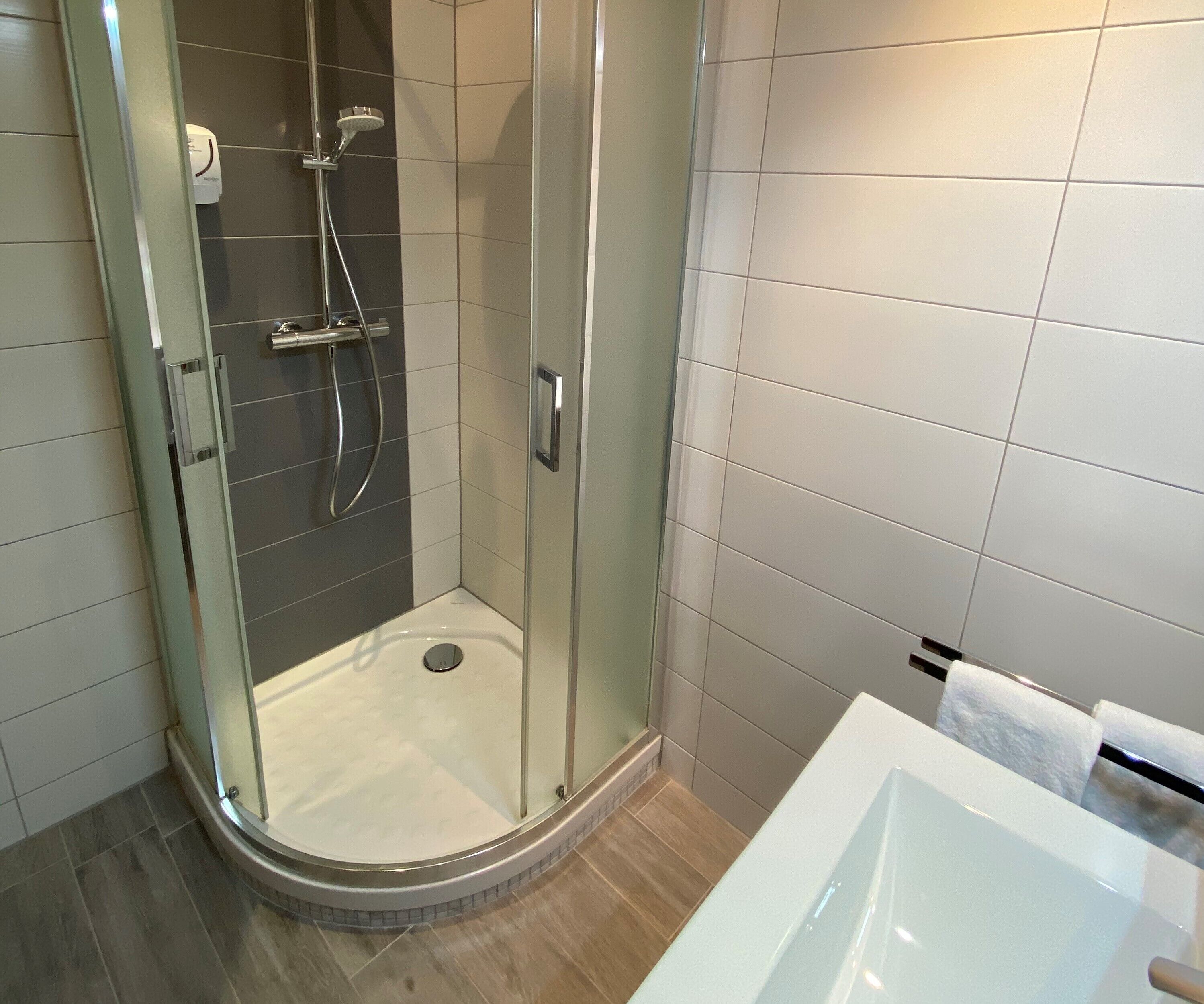 Un baño moderno con ducha envuelta en vidrio, una bañera blanca y suelo de baldosas.