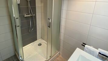 Un baño moderno con ducha envuelta en vidrio, una bañera blanca y suelo de baldosas.