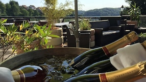 Un seau rempli de bouteilles de champagne et de glace, placé sur une terrasse aménagée avec du mobilier d’extérieur et des plantes en pot.