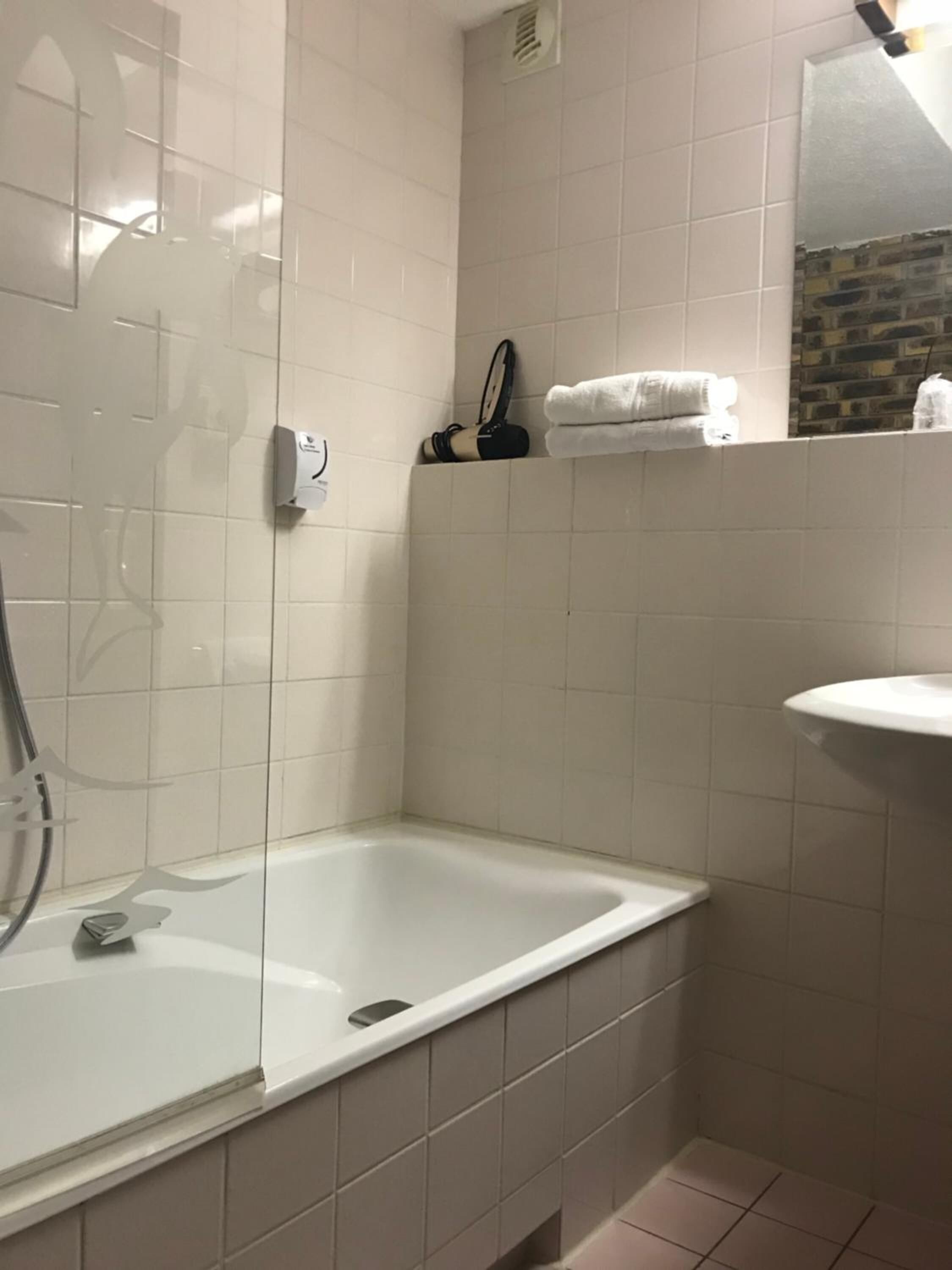 Een badkamer met een douchecabine van glas, een witte wastafel en een handdoekrek met opgevouwen handdoeken.