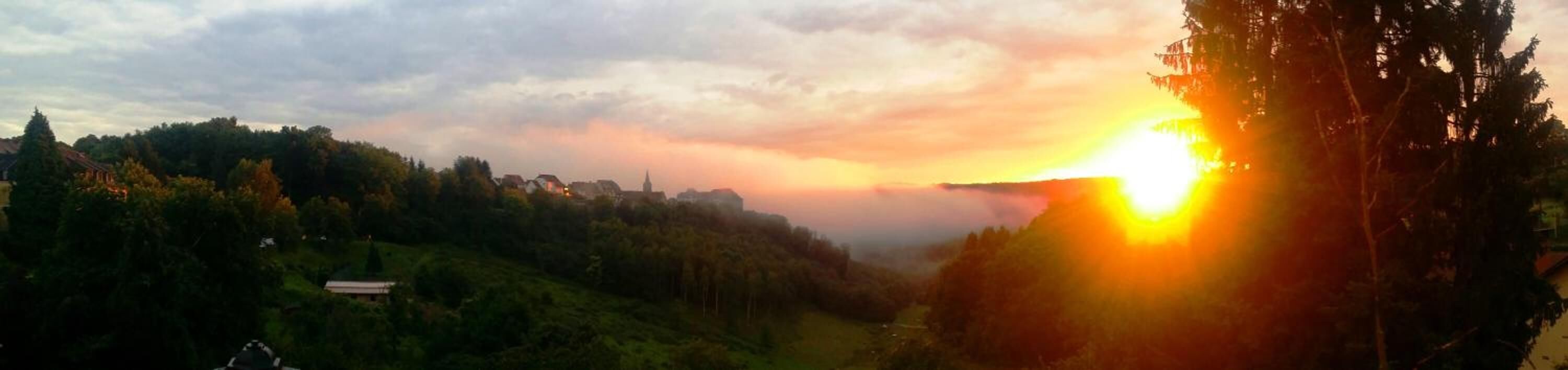 Un coucher de soleil sur une vallée, avec des bâtiments et des arbres.