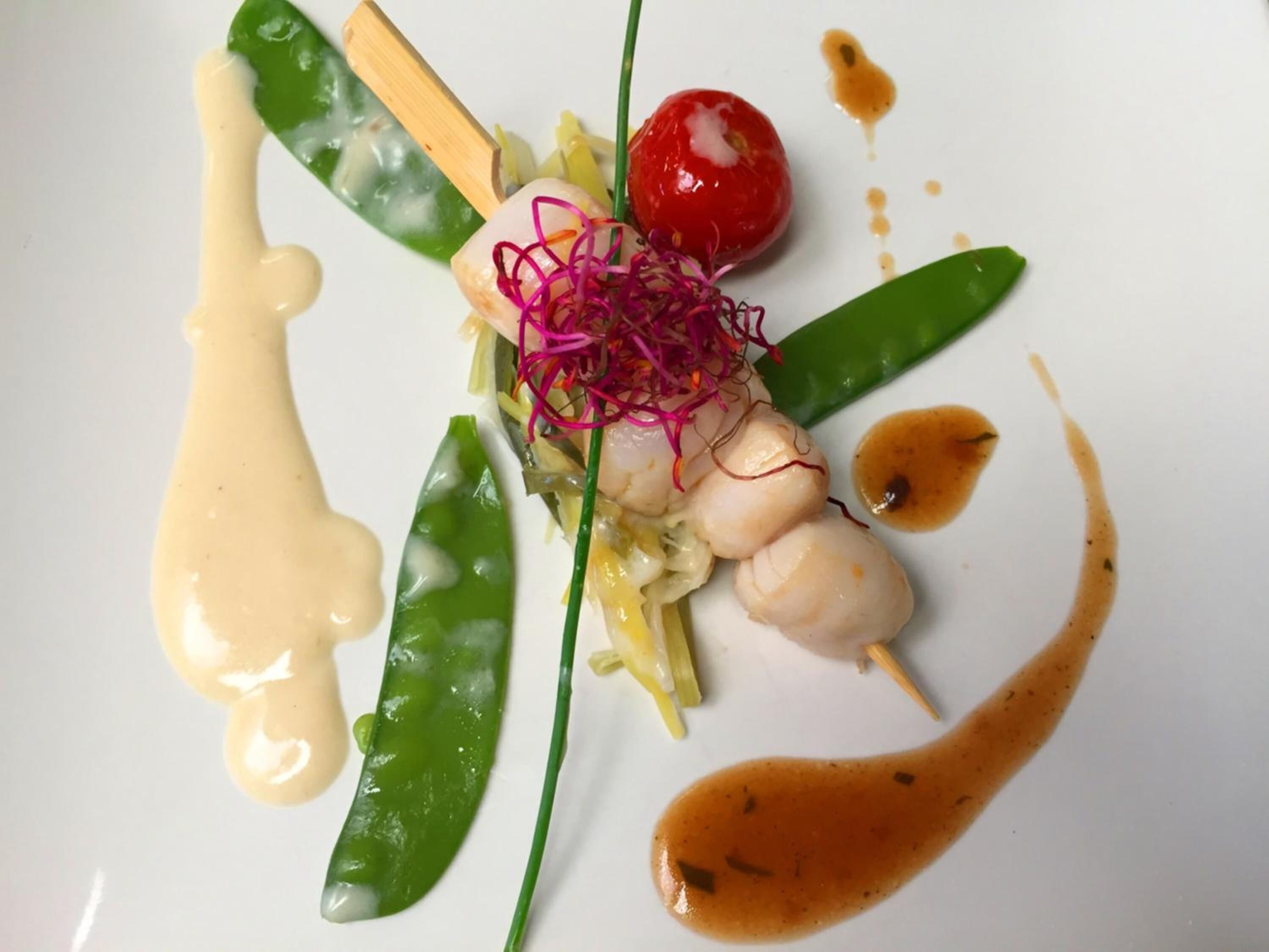 A plate with various food items including scallops, green peas, and a cherry tomato, arranged artistically.