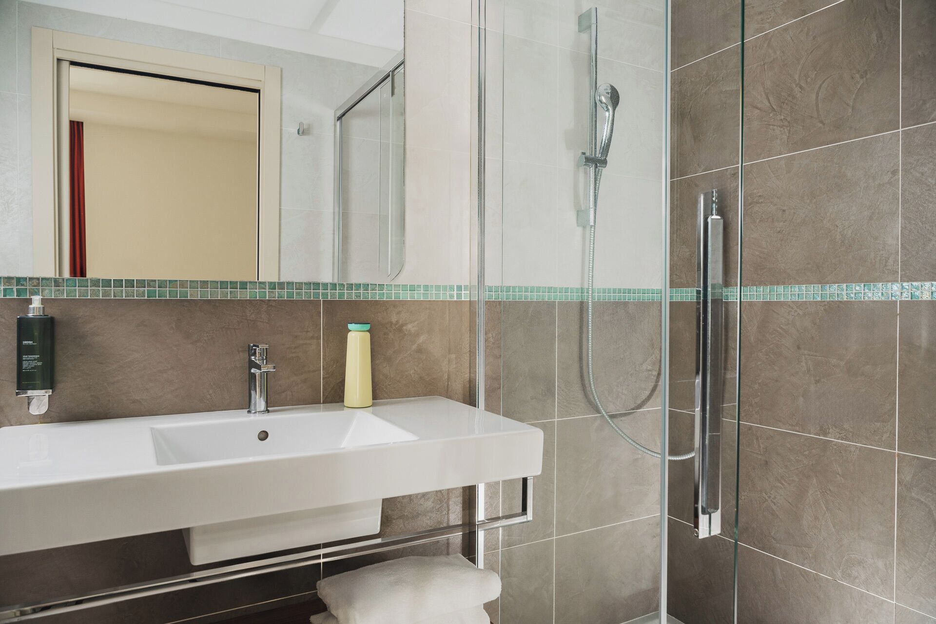 Un baño moderno con un lavabo blanco, cabina de ducha de vidrio y un espejo sobre el lavabo.