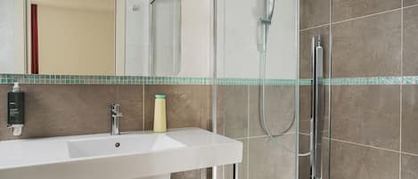 Un baño moderno con un lavabo blanco, cabina de ducha de vidrio y un espejo sobre el lavabo.