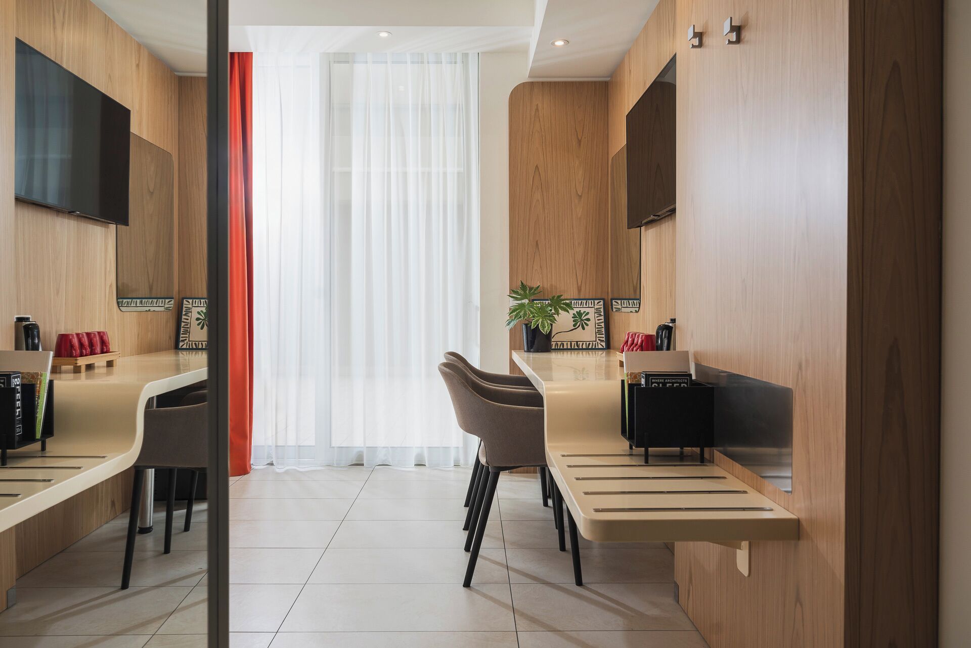 Una habitación moderna y luminosa con una mesa larga, dos sillas, una planta en maceta y un televisor de pantalla plana montado en la pared.