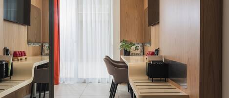A modern, well-lit room with a long table, two chairs, a potted plant, and a flat-screen TV mounted on the wall.