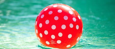 A red polka-dotted ball floating in water.