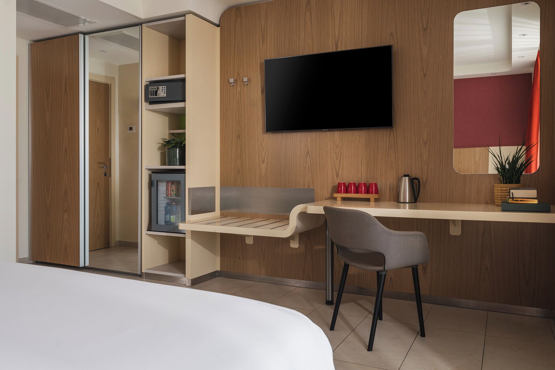 Una habitación de hotel con cama, escritorio, silla, televisor, minibar y armario.