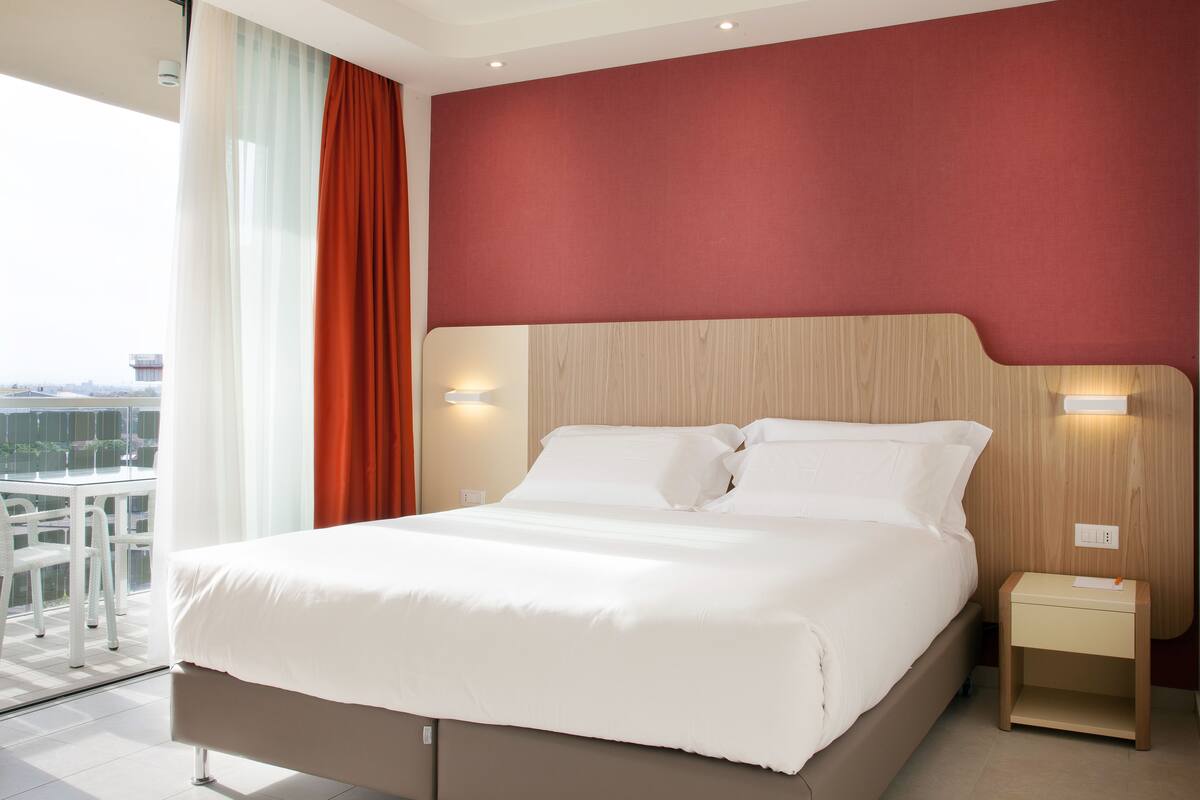 Une chambre d’hôtel moderne dotée d’un grand lit, d’une tête de lit en bois, de deux tables de chevet et offrant une vue sur la ville grâce à de grandes fenêtres.