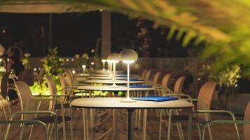 Un área de comedor al aire libre con mesas y sillas, bajo un toldo.