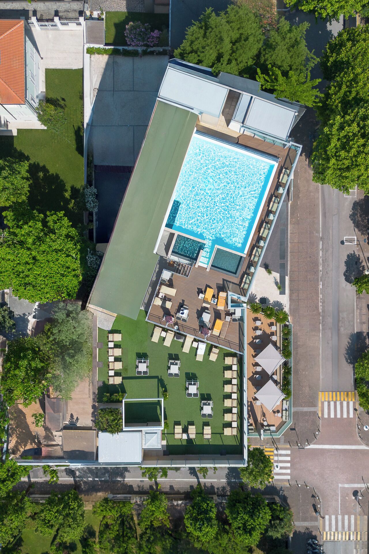 An aerial view of a hotel with a rooftop pool, outdoor seating area, and a landscaped garden.