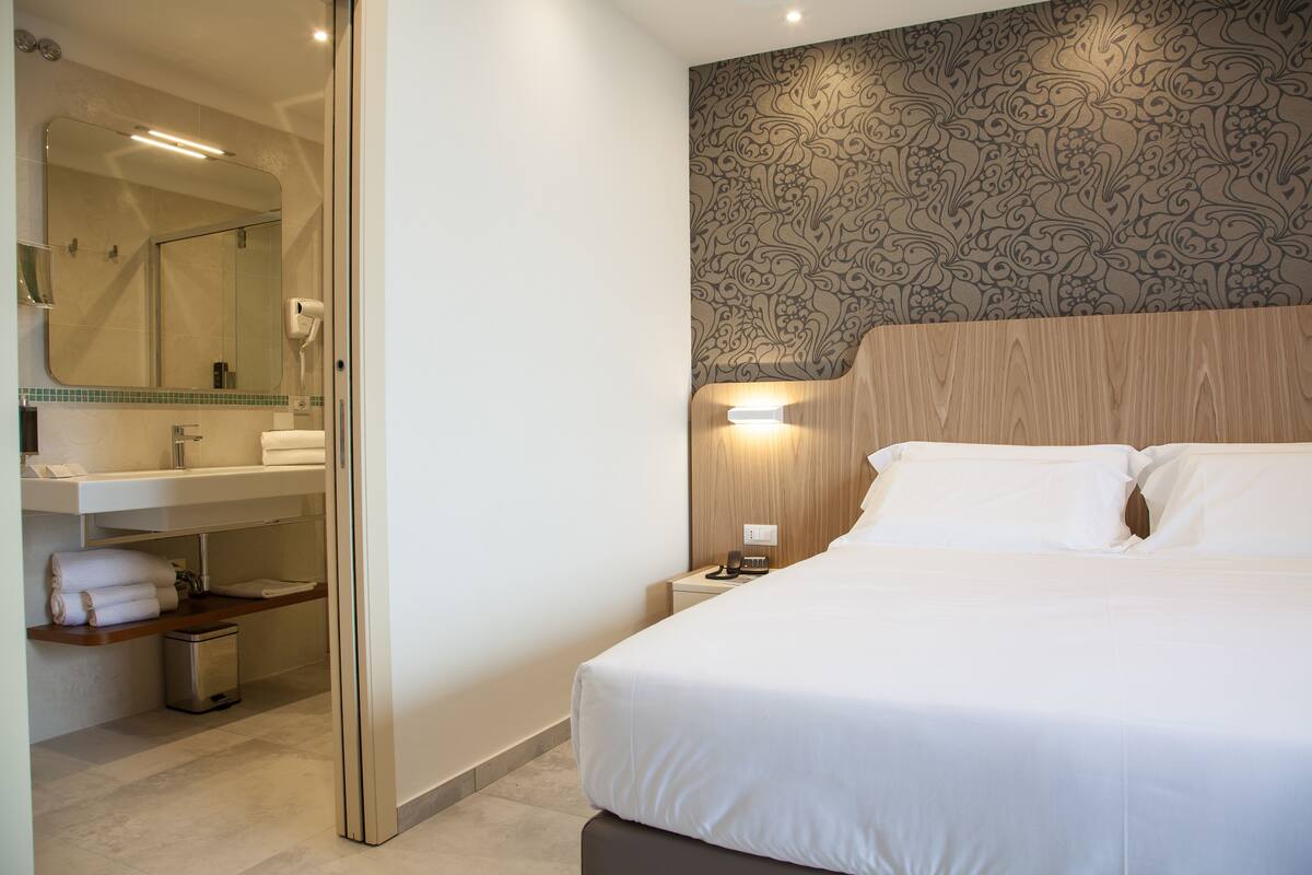 Une chambre d’hôtel avec un grand lit, une salle de bain équipée d’un miroir, d’un lavabo et d’un porte-serviettes.