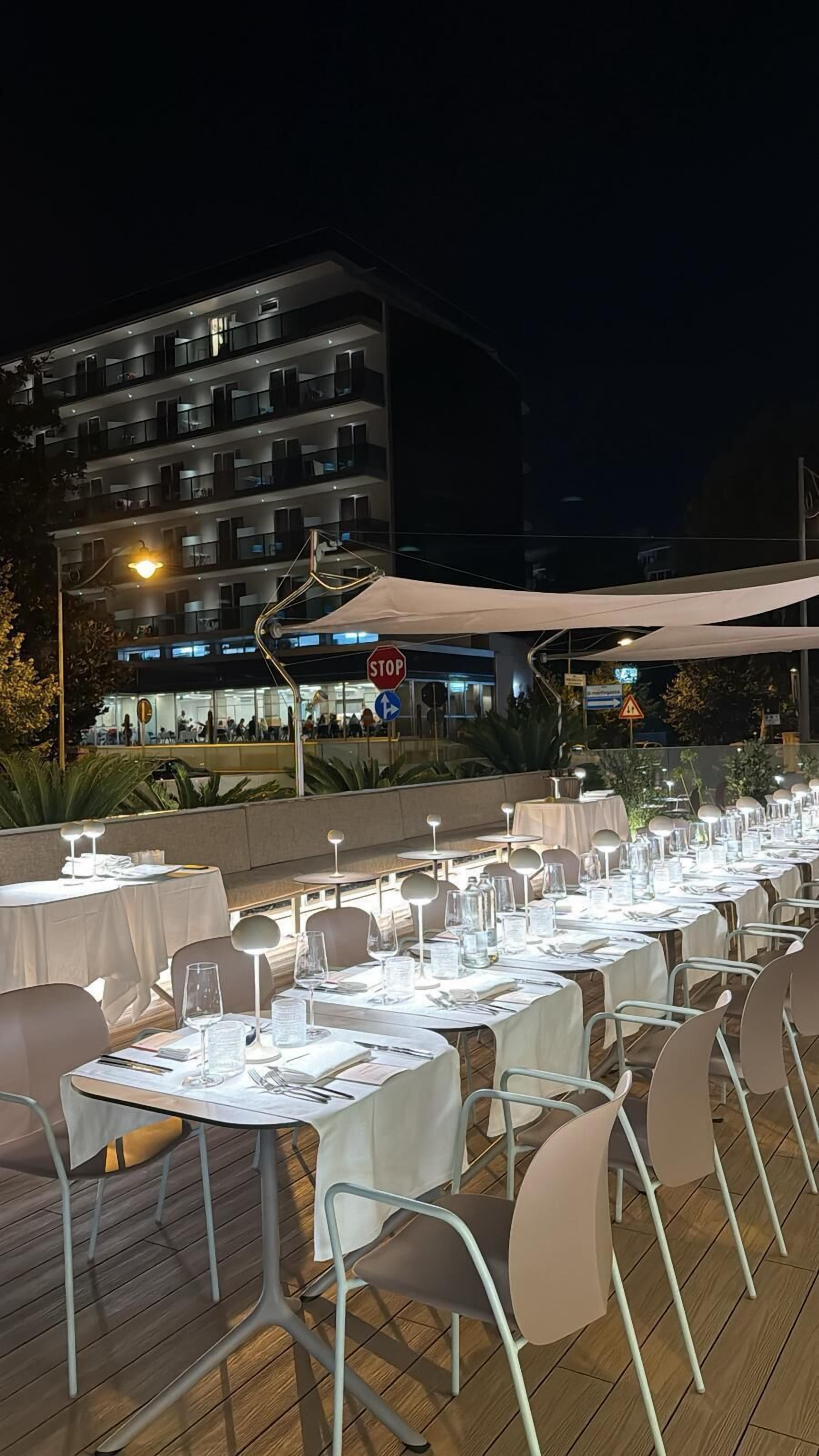 An outdoor dining area with tables set for a meal, a stop sign, and a building with illuminated windows in the background.