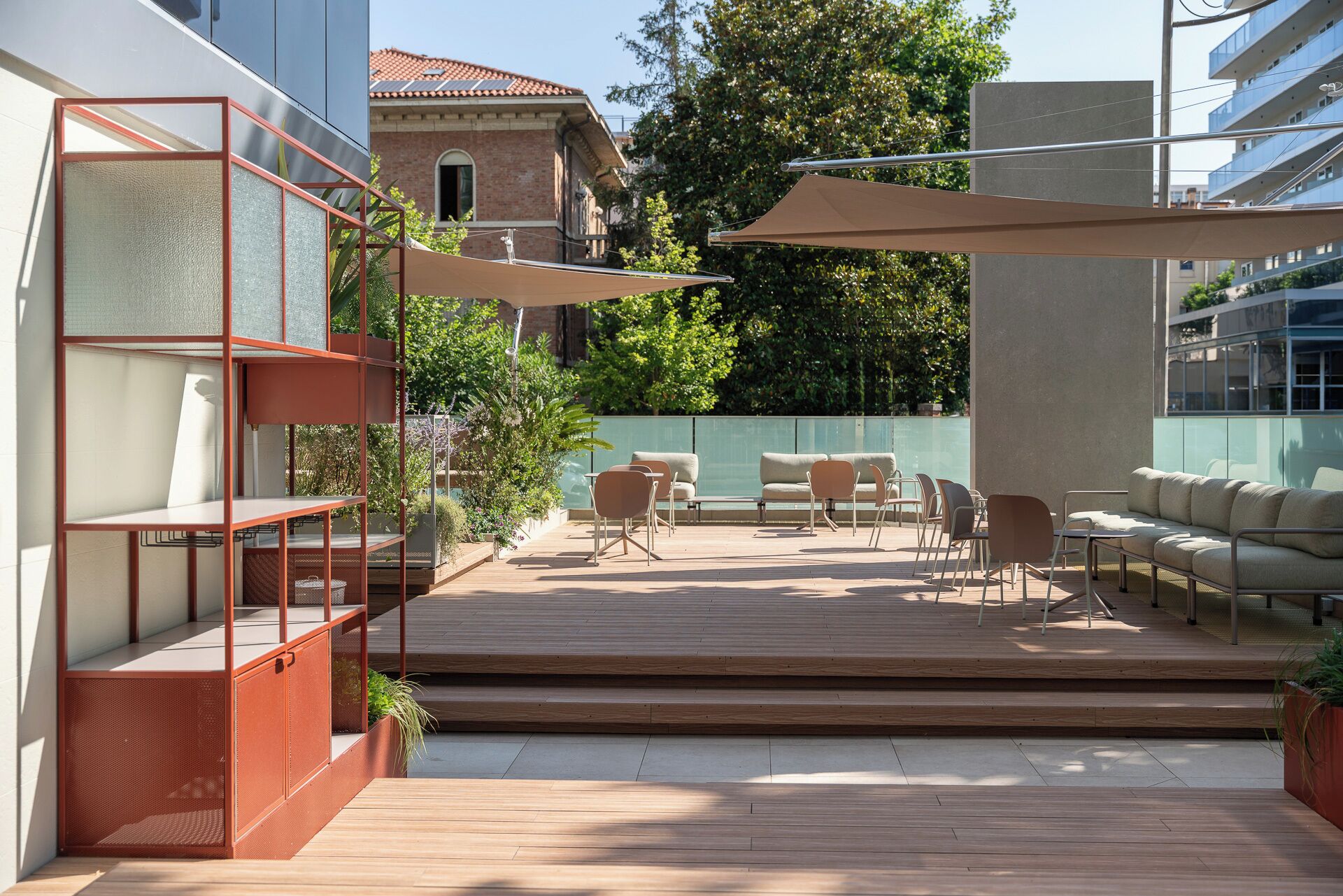 A modern outdoor patio with wooden flooring, a seating area with sofas and chairs, and a metal shelving unit with cushions.