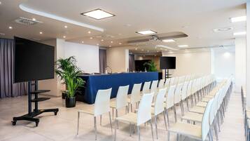 A conference room with a long table, white chairs, a large screen, and a plant.