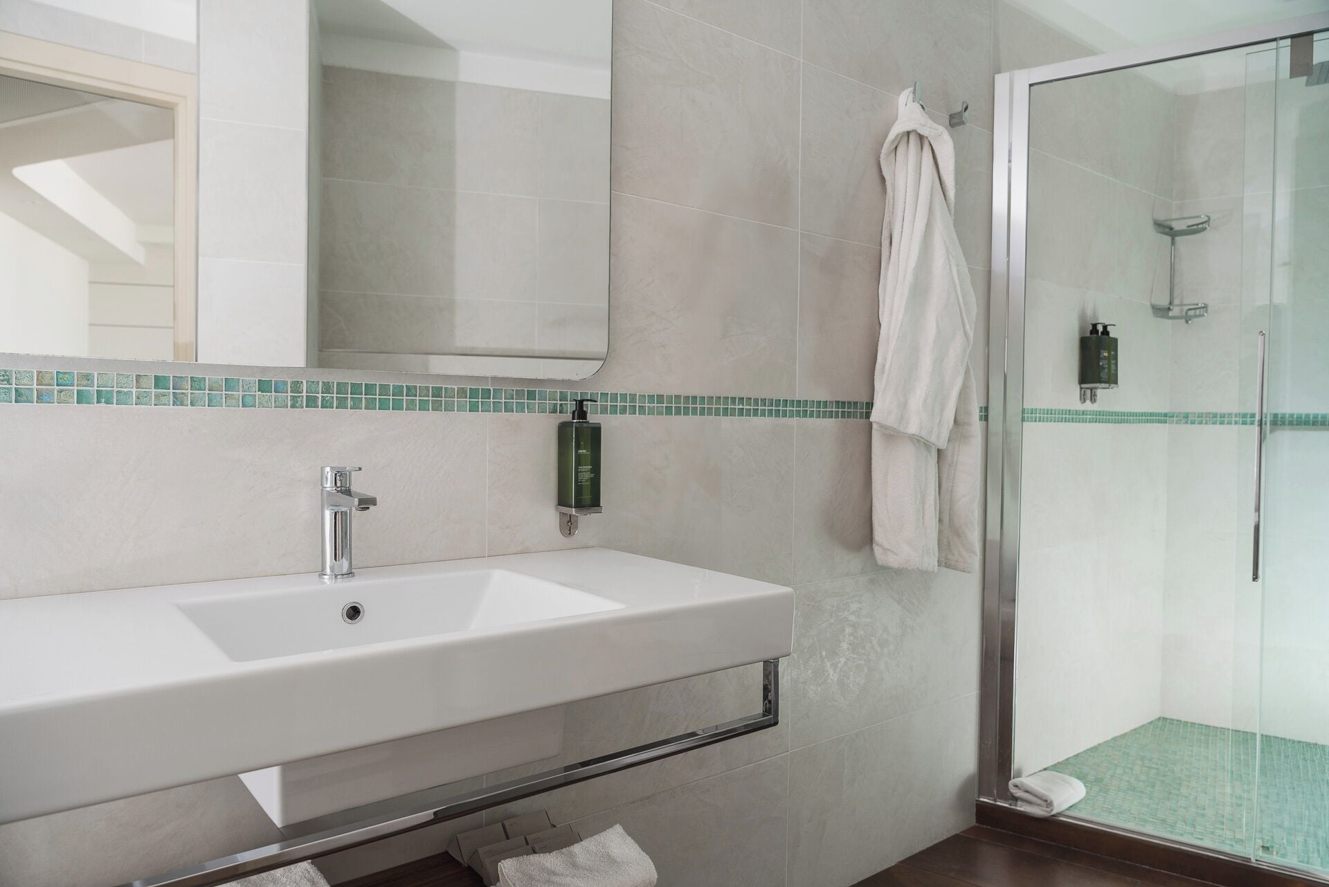 A modern bathroom with a white sink, a glass shower enclosure, and a towel hanging on the wall.