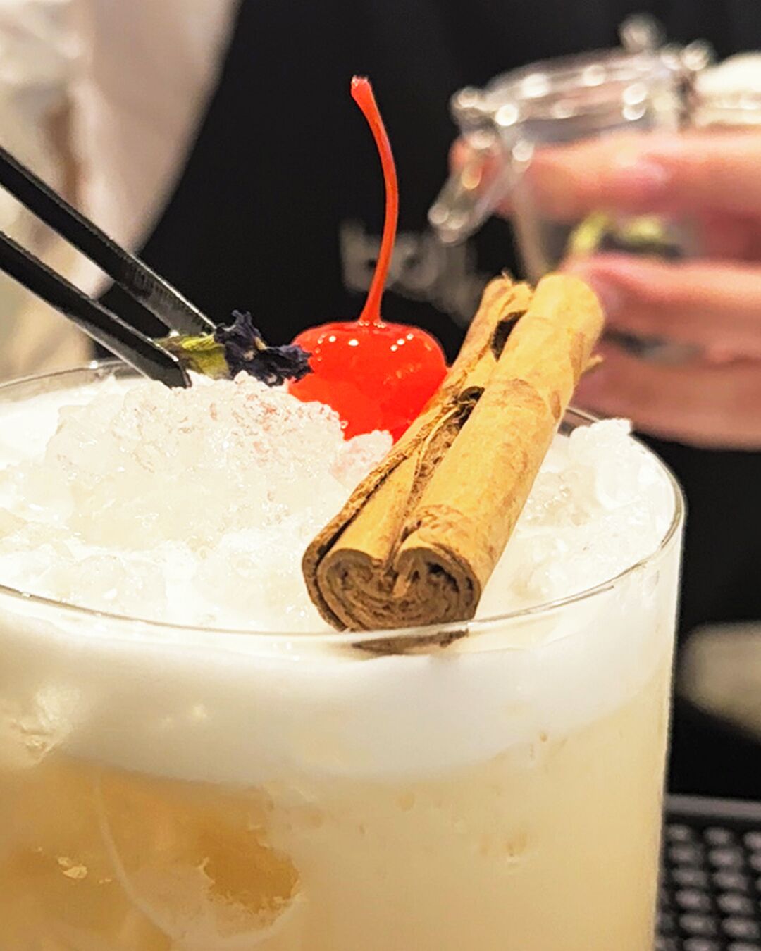 Een cocktail met ijs, een stokje kaneel en een kers.