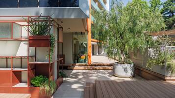 A modern outdoor space with a wooden deck, a large potted plant, and a metal structure with plants.
