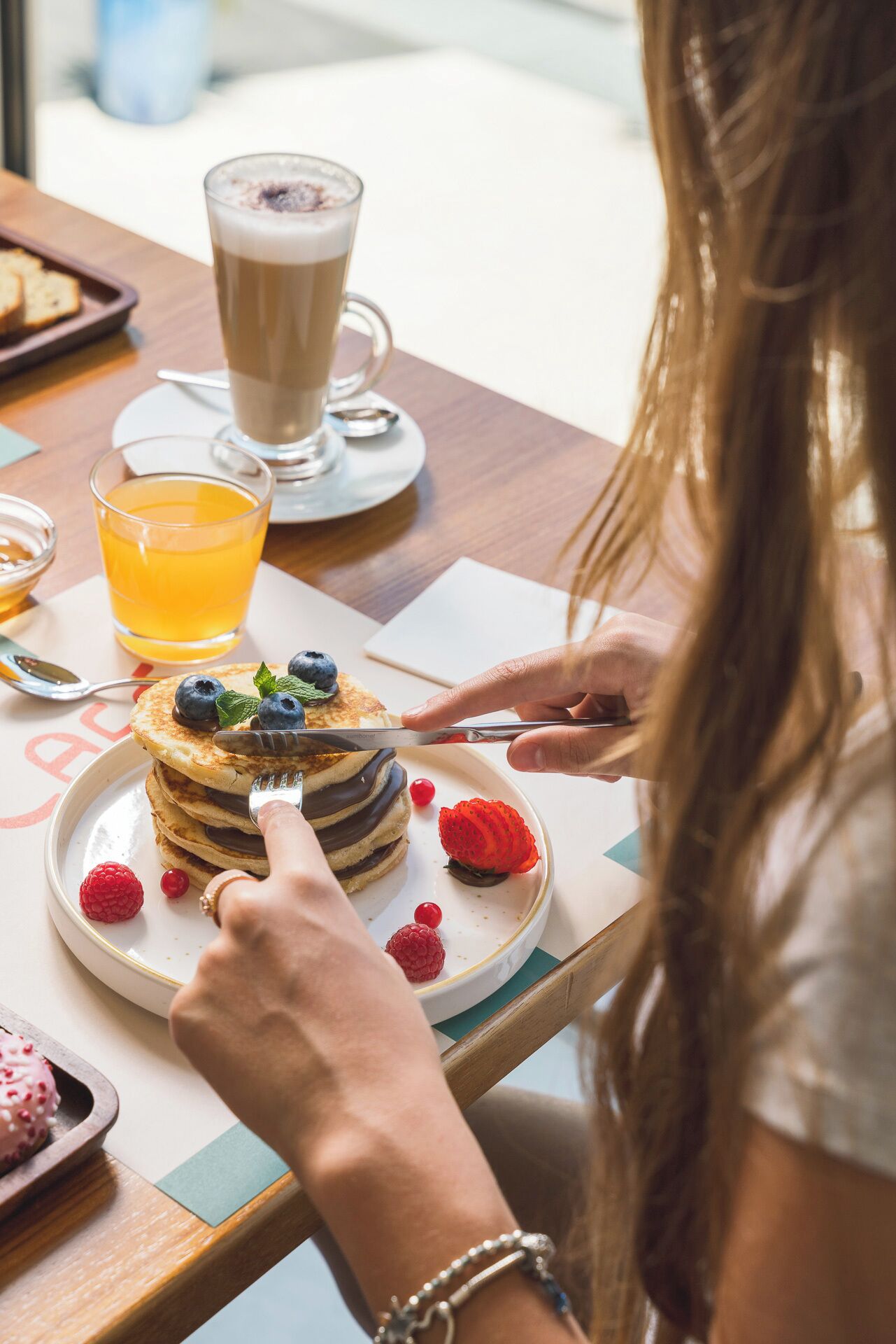 A person cutting a stack of pancakes topped with blueberries and raspberries, with a glass of orange juice and a cup of coffee on the table.