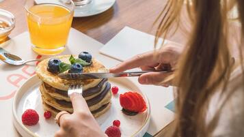 A person cutting a stack of pancakes topped with blueberries and raspberries, with a glass of orange juice and a cup of coffee on the table.