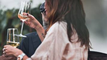 Uma pessoa segurando uma taça de vinho, outra pessoa com uma tatuagem no braço e uma bolsa com padrão xadrez.