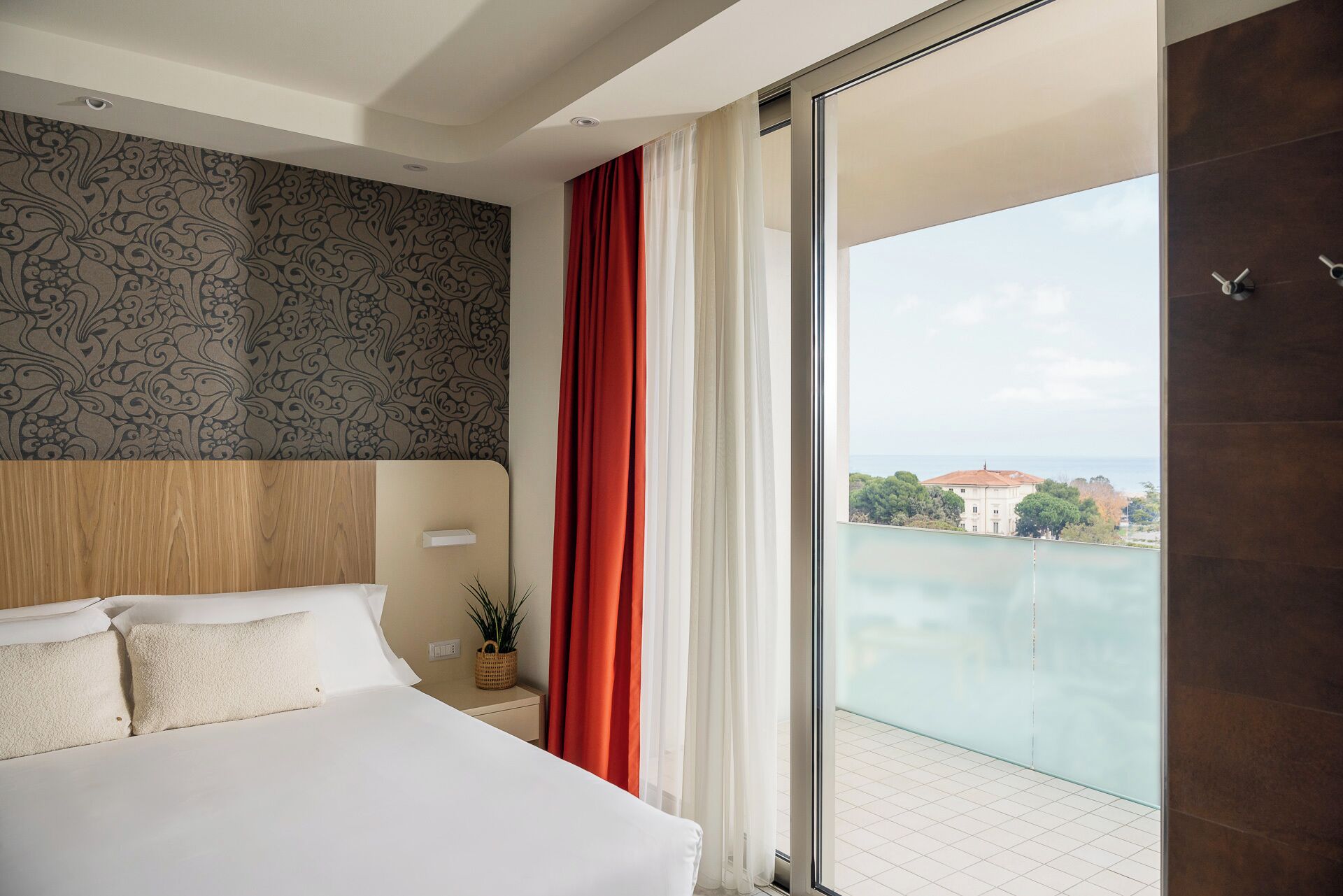 Ein Hotelzimmer mit einem großen Bett, Meerblick und einem Balkon mit Glastür.