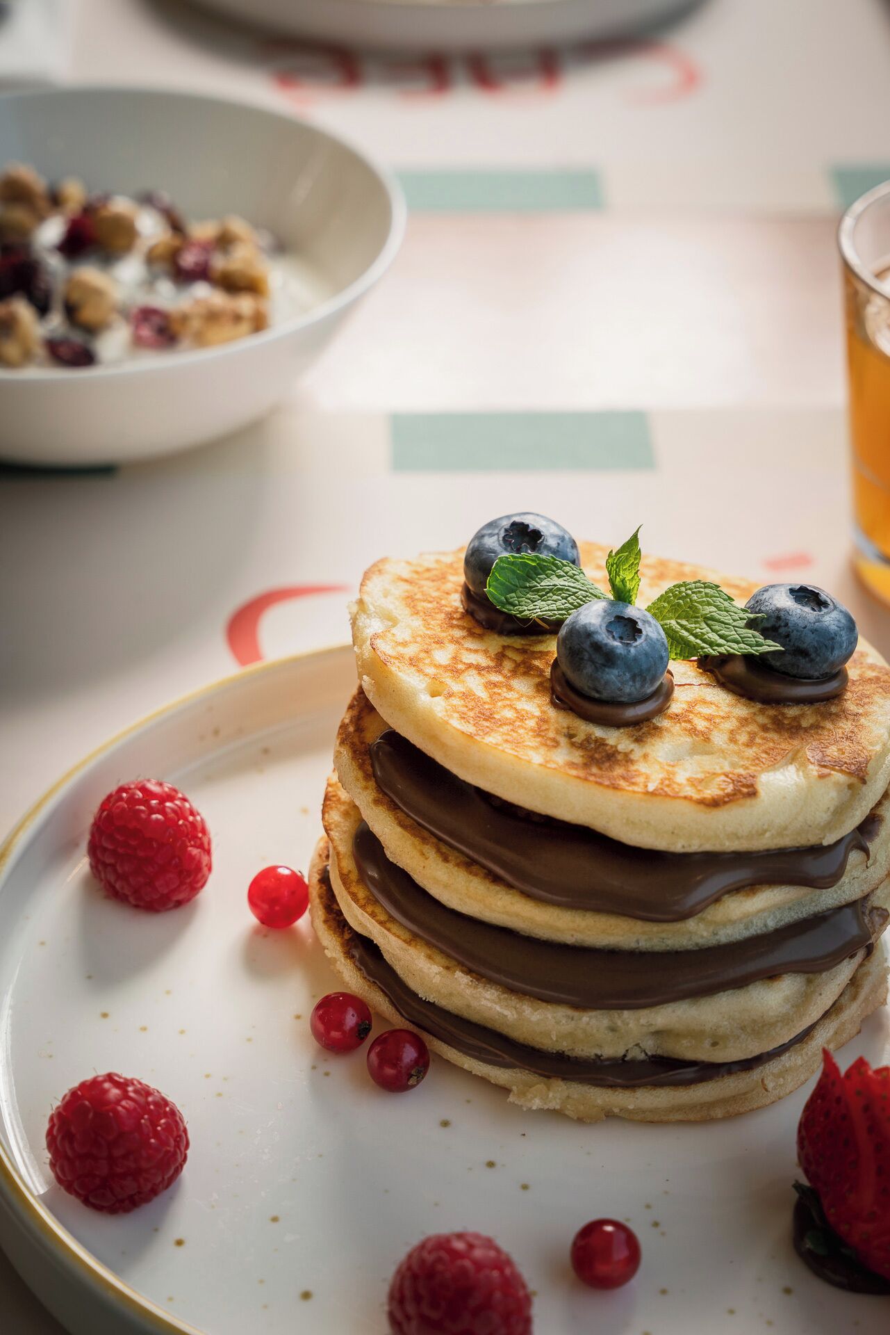 A stack of pancakes with chocolate spread and fresh berries on a plate.