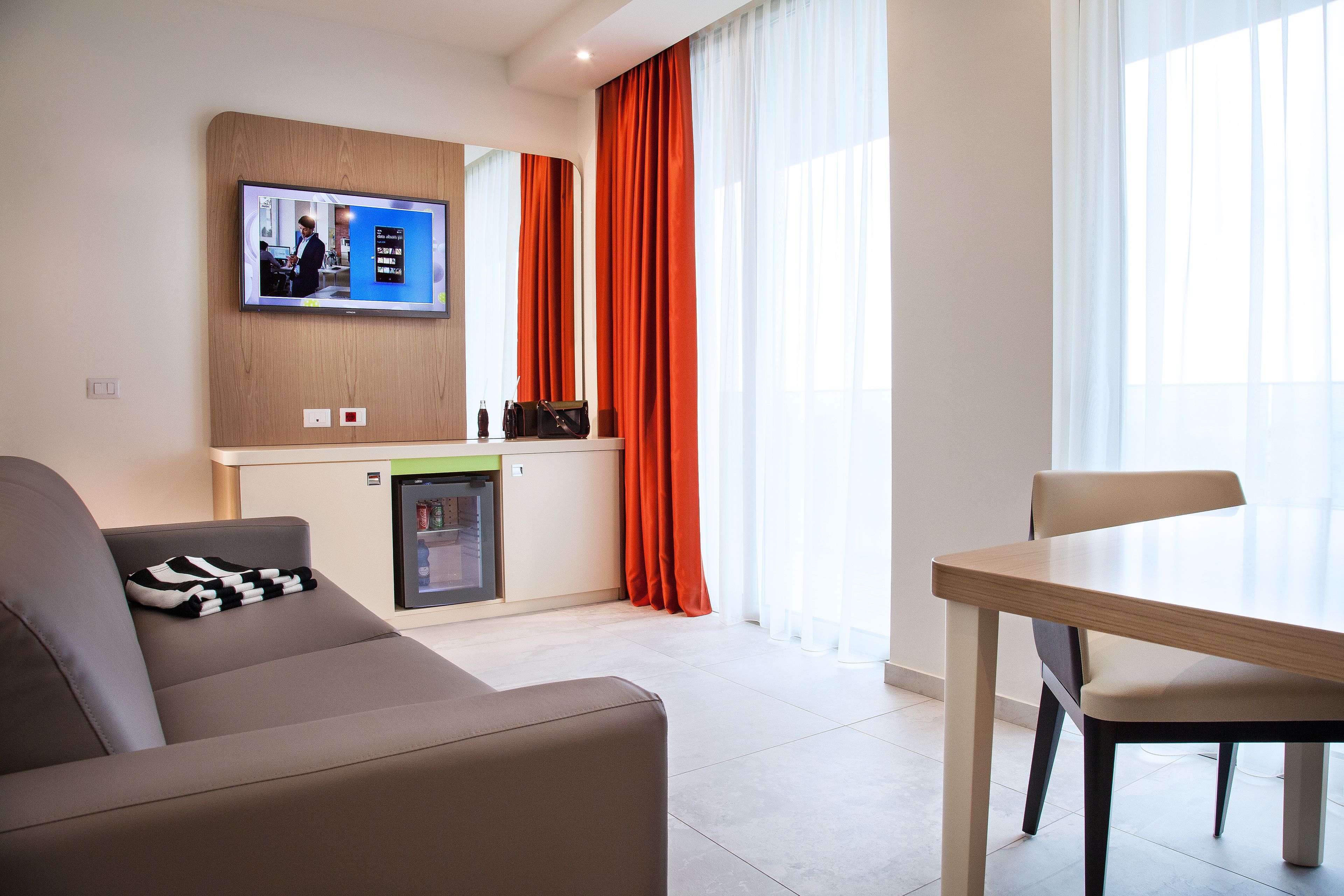 A modern living room with a sofa, a dining table, and a kitchen area with a TV mounted on the wall.