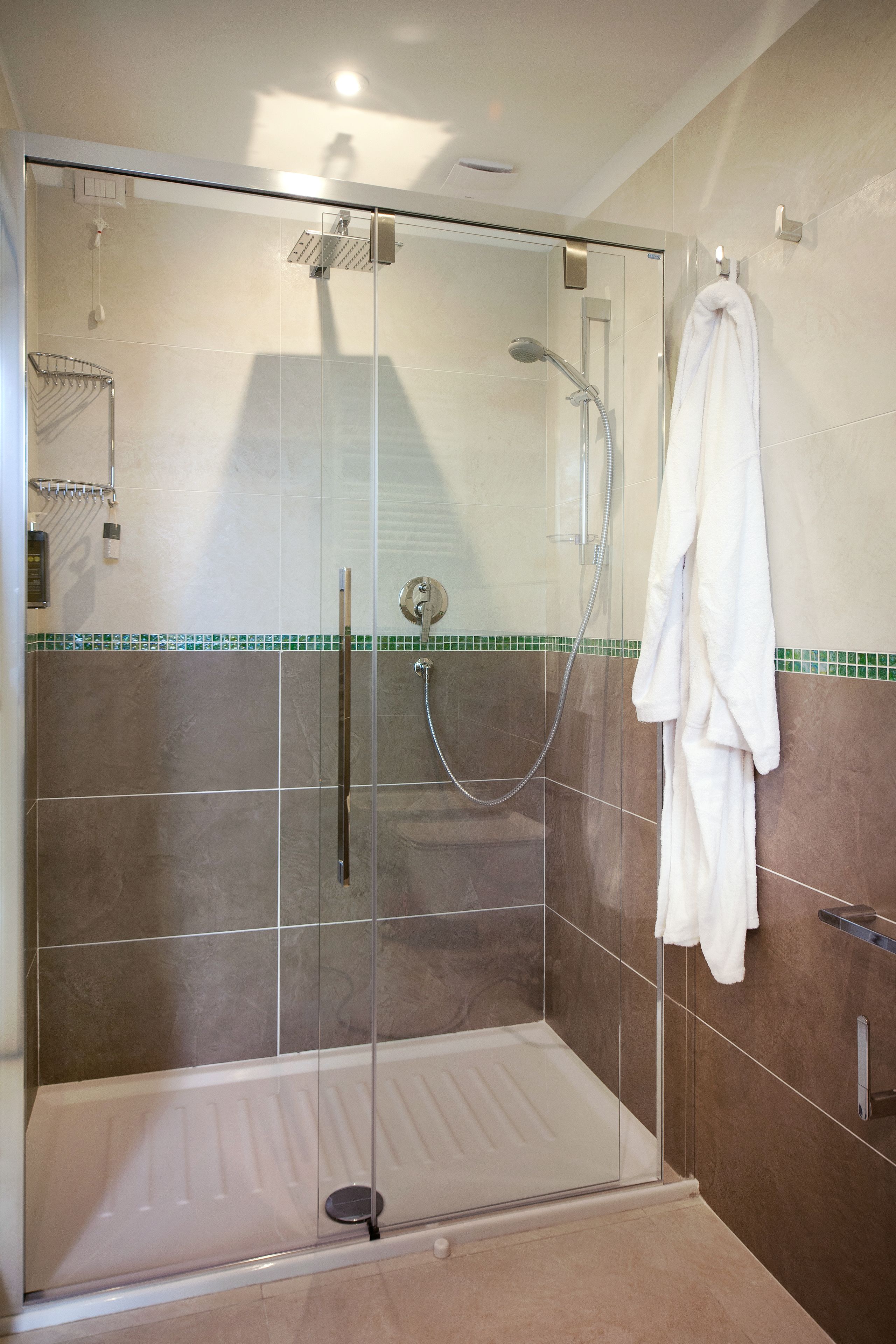 Une douche à l’italienne avec une porte en verre, une serviette blanche accrochée au mur et un sol carrelé de couleurs vert et beige.