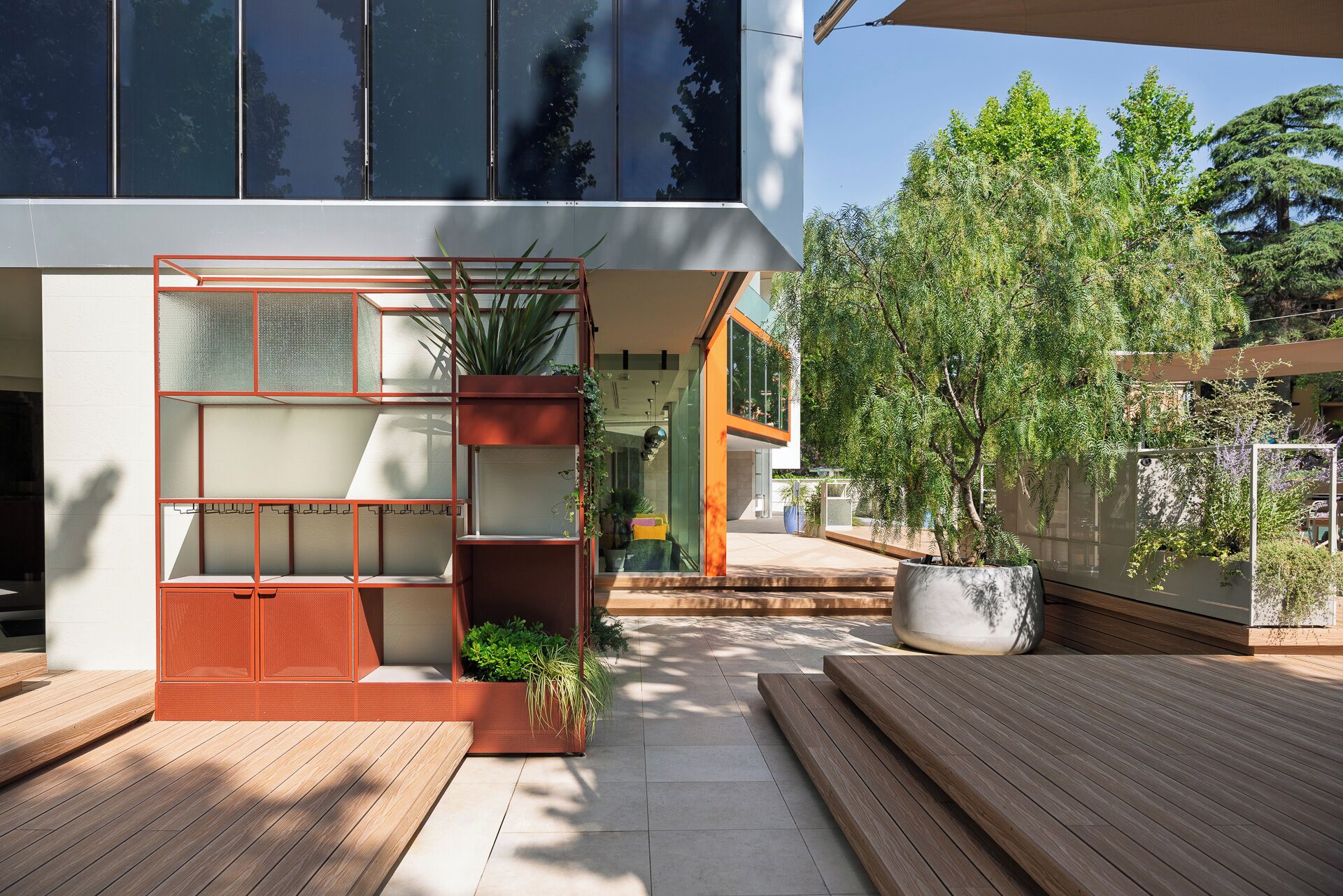 Un bâtiment moderne doté d’une façade en verre, d’une terrasse en bois et de plantes en pot.