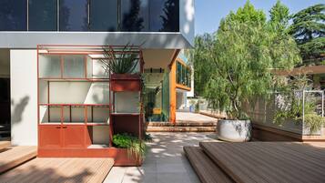 A modern building with a glass facade, outdoor wooden deck, and potted plants.