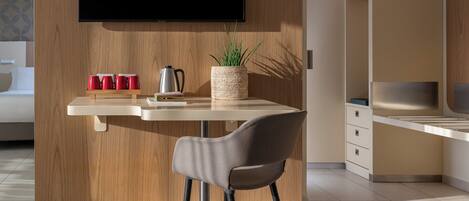 A modern kitchen with a wooden accent wall, a flat-screen TV mounted above a white countertop, and a chair with a grey cushion.