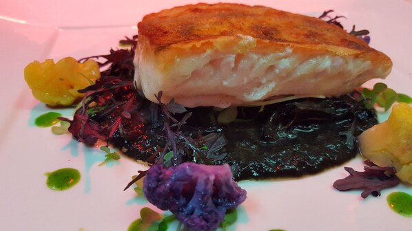 A plate of food with a piece of fish on top of a dark vegetable, surrounded by colorful garnishes.