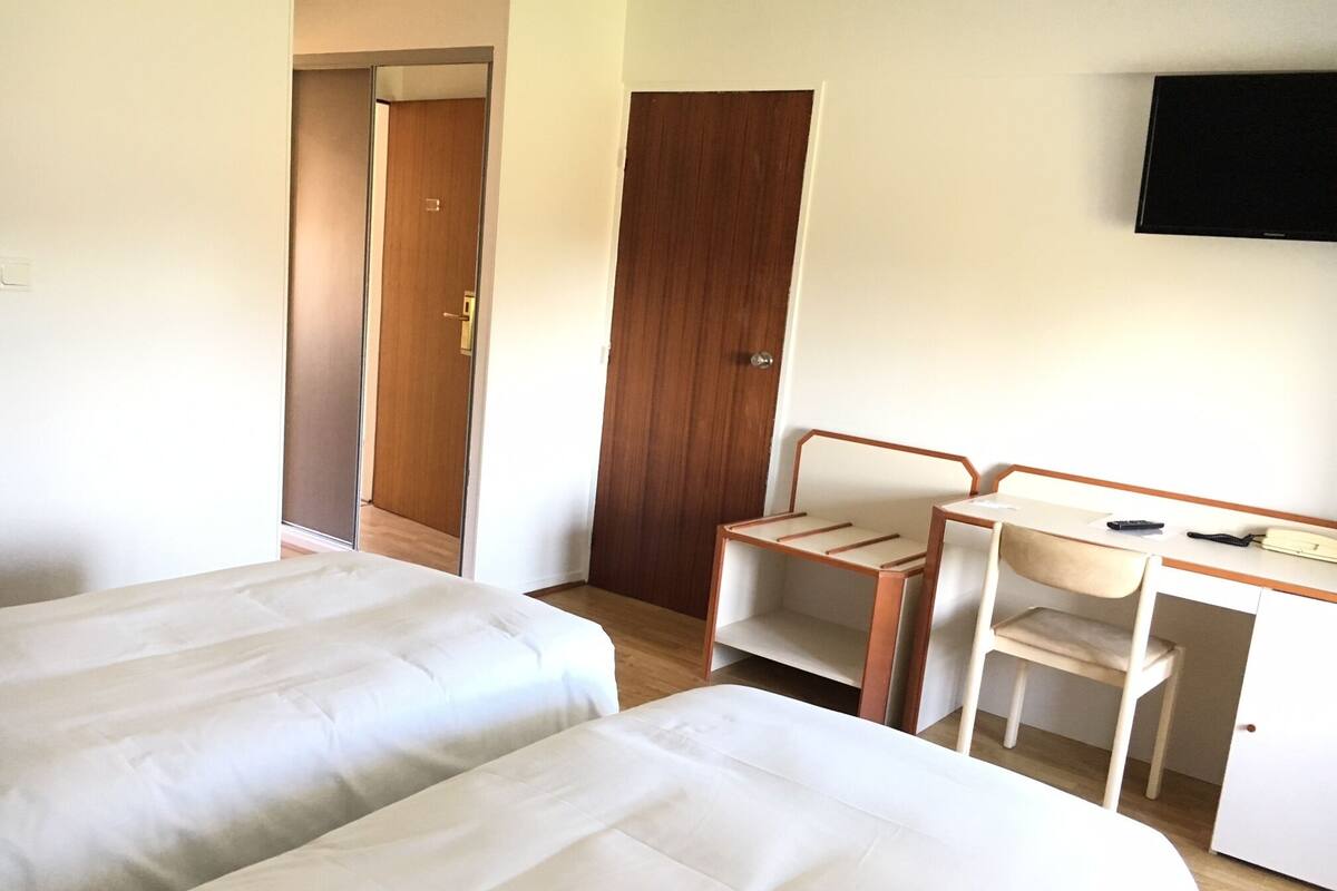 Una camera d'albergo con due letti, una scrivania, una sedia e una TV a parete.