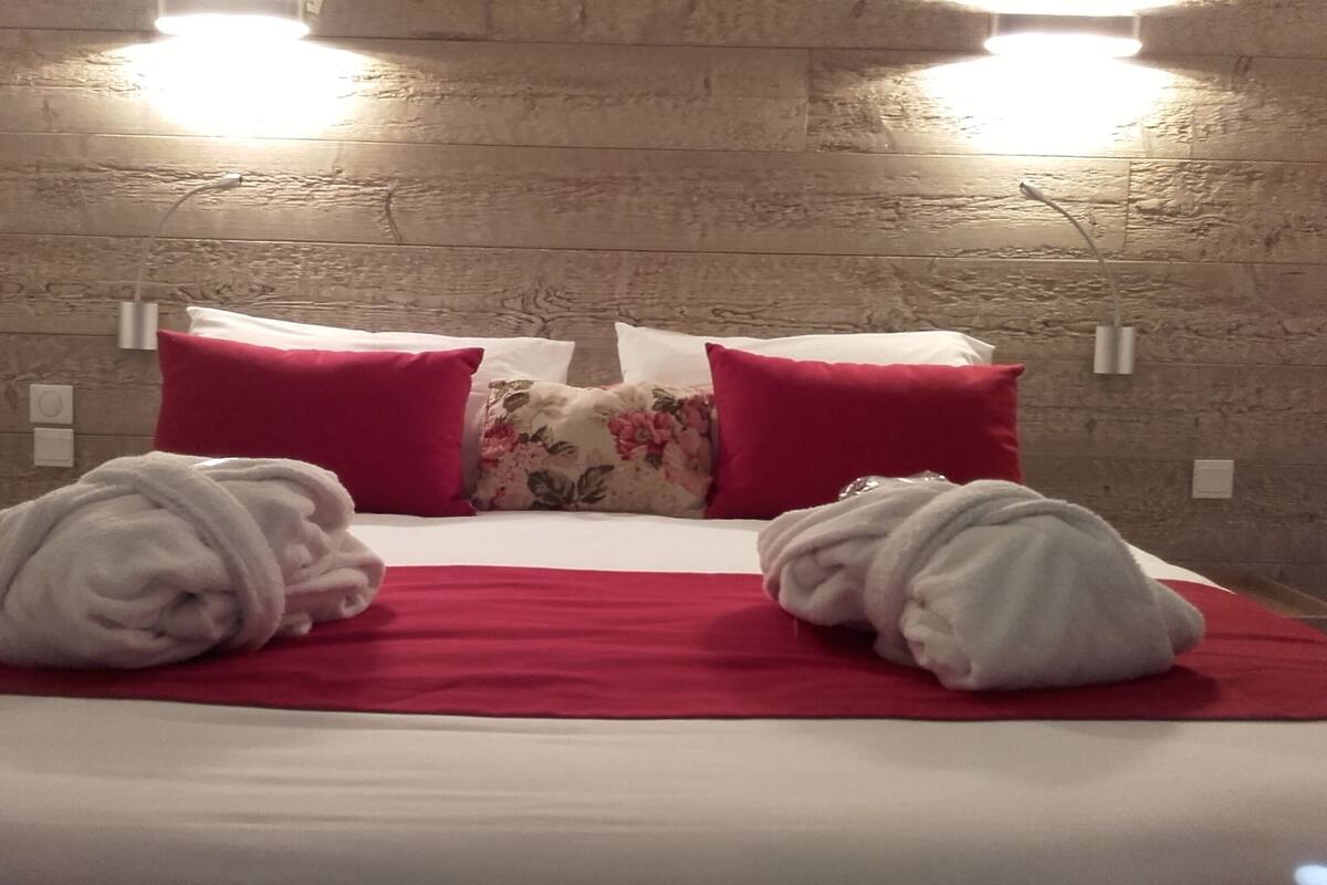 Letto rifatto con lenzuola rosse e bianche, due cuscini rossi e un cuscino con motivo floreale. Ci sono due asciugamani bianchi sul letto.