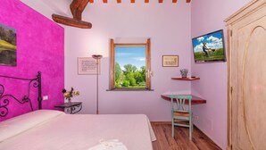 A bedroom with a bed, a window with a view of greenery, a desk with a chair, and a wardrobe.