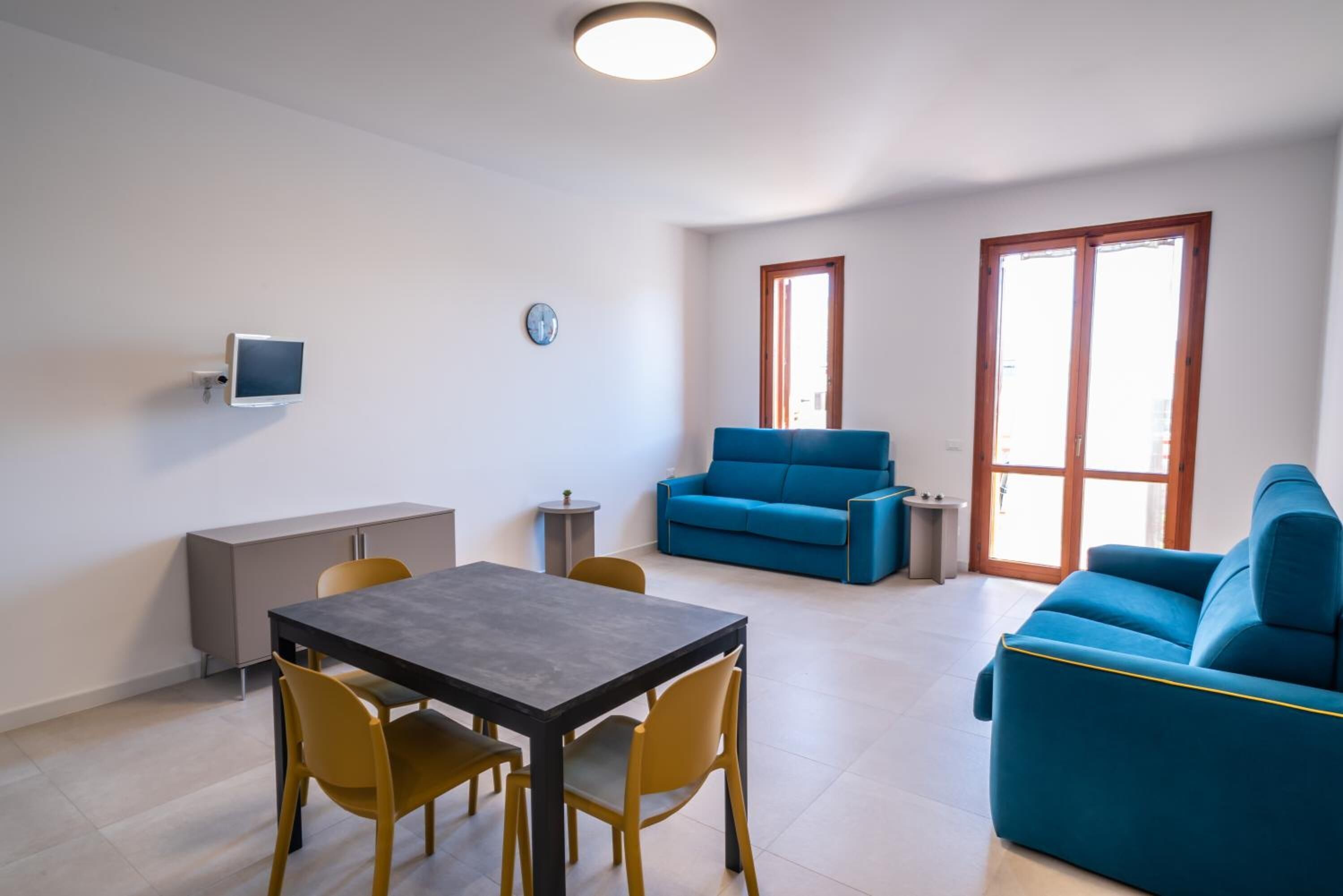 Sala de estar moderna com área de jantar, um sofá azul e uma TV fixada na parede.