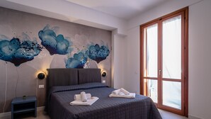 A bedroom with a large bed, a nightstand, a wall mural, and a sliding glass door. - Residence Marinella (San Vito Lo Capo)