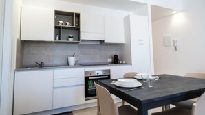 A modern kitchen with white cabinetry, a built-in oven, and a dining area with a table and chairs. - Residence Marinella (San Vito Lo Capo)
