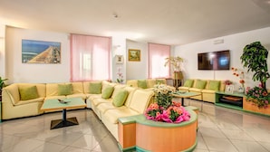 Un salon moderne avec un canapé beige, un comptoir d’accueil en bois et un téléviseur fixé au mur.