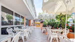 Une terrasse extérieure avec des chaises et des tables en plastique blanc, des parasols et des plantes en pot.