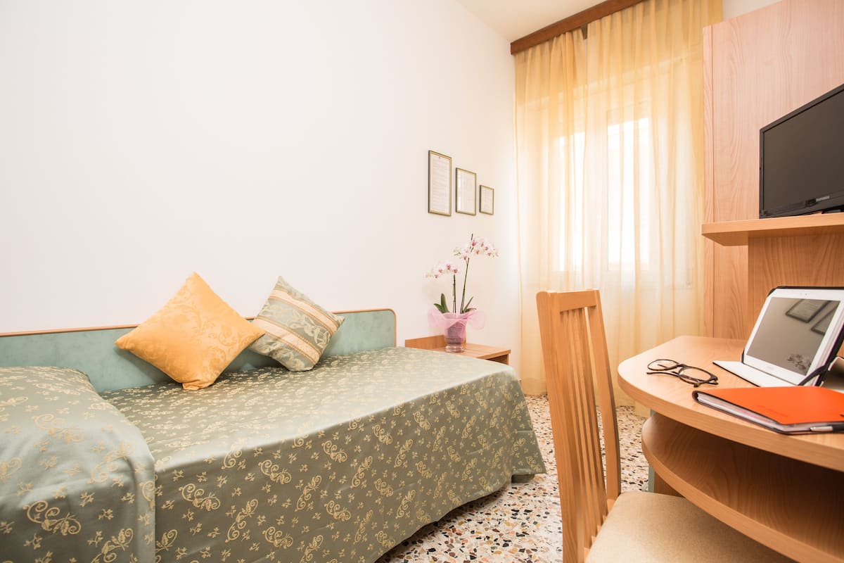 A hotel room with a bed, a desk with a laptop, a TV, and a chair.