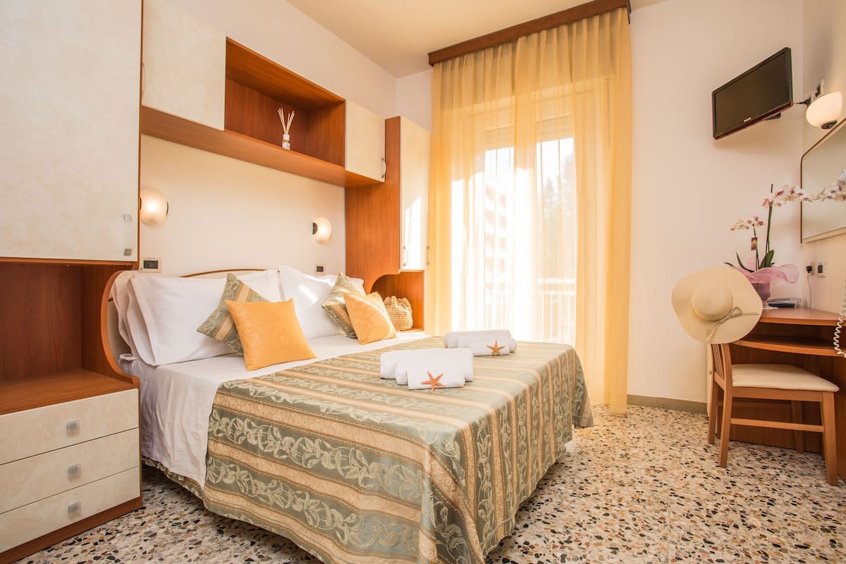 A hotel room with a bed, a desk, a chair, a television, and a window with curtains.