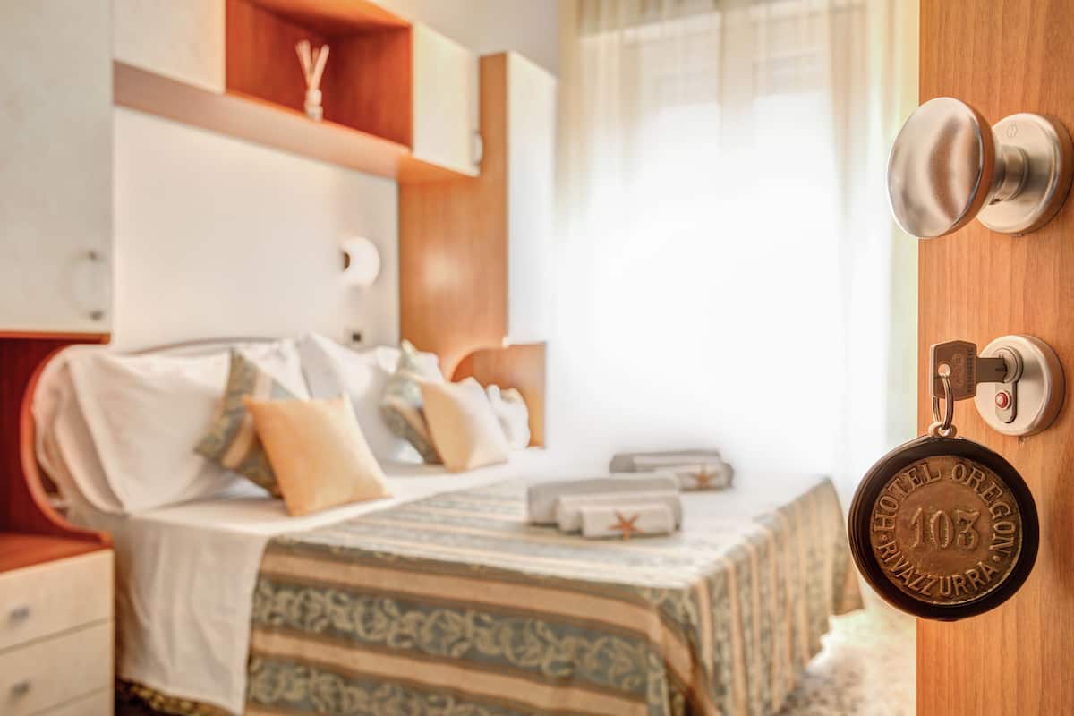 A hotel room with a bed, a bedside table, a wardrobe, and a door with a keycard lock.