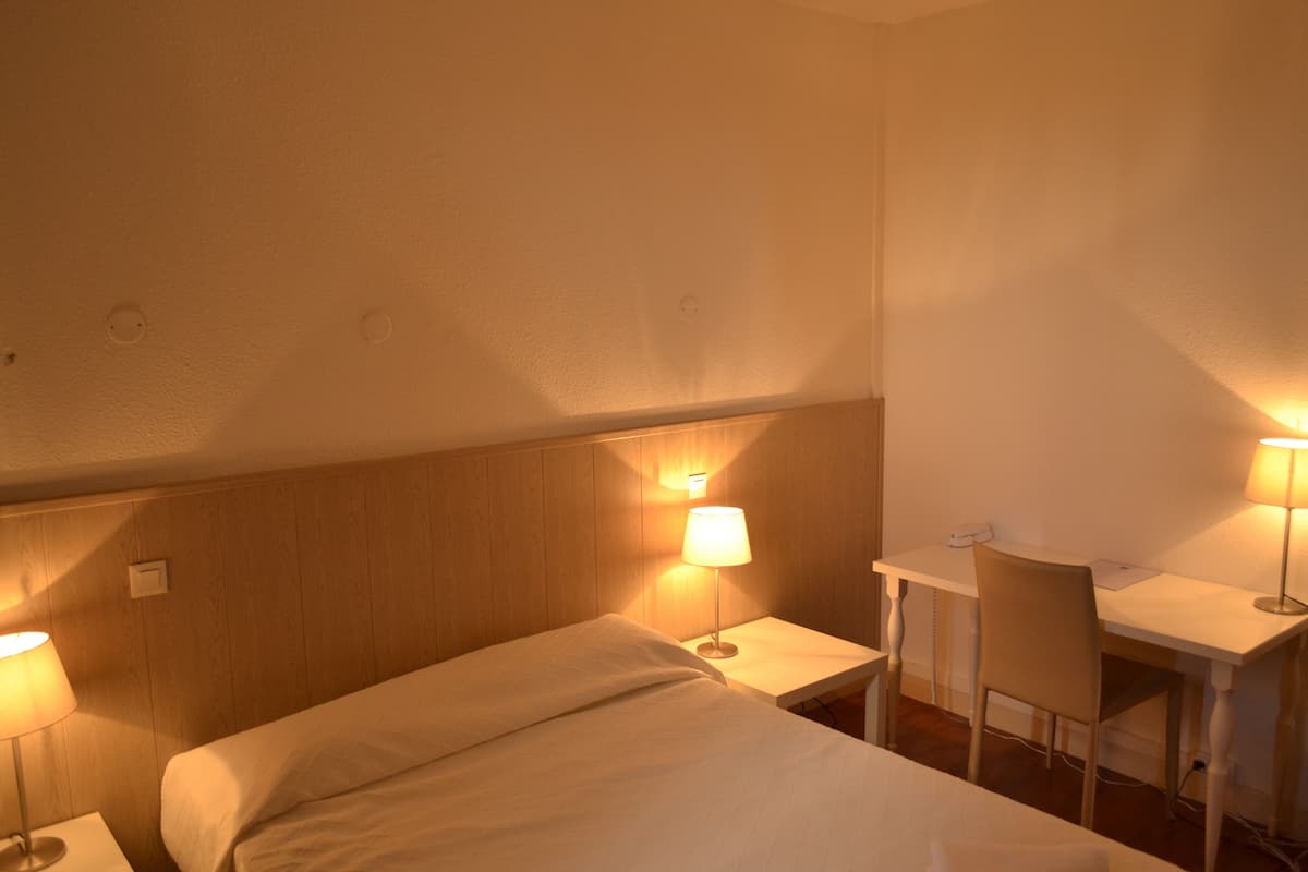 A hotel room with a bed, a desk, and two lamps.
