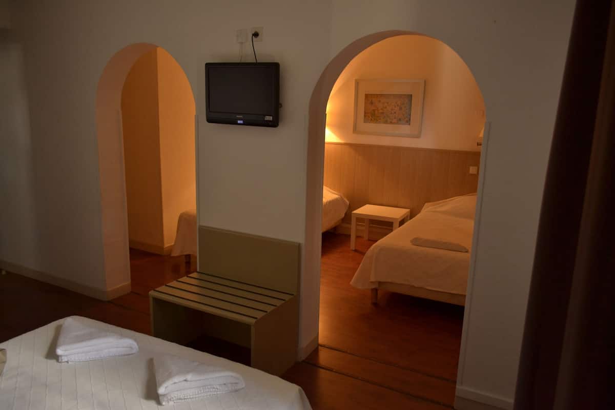 A hotel room with a bed, a bench, a TV, and two archways leading to another room.
