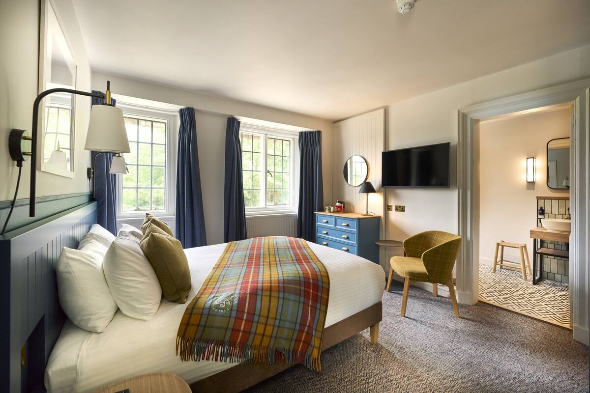 Ein Hotelzimmer mit Bett, Sessel, Fernseher, Kommode und einem durchgegangenen Tür sichtbar liegenden Badezimmer.