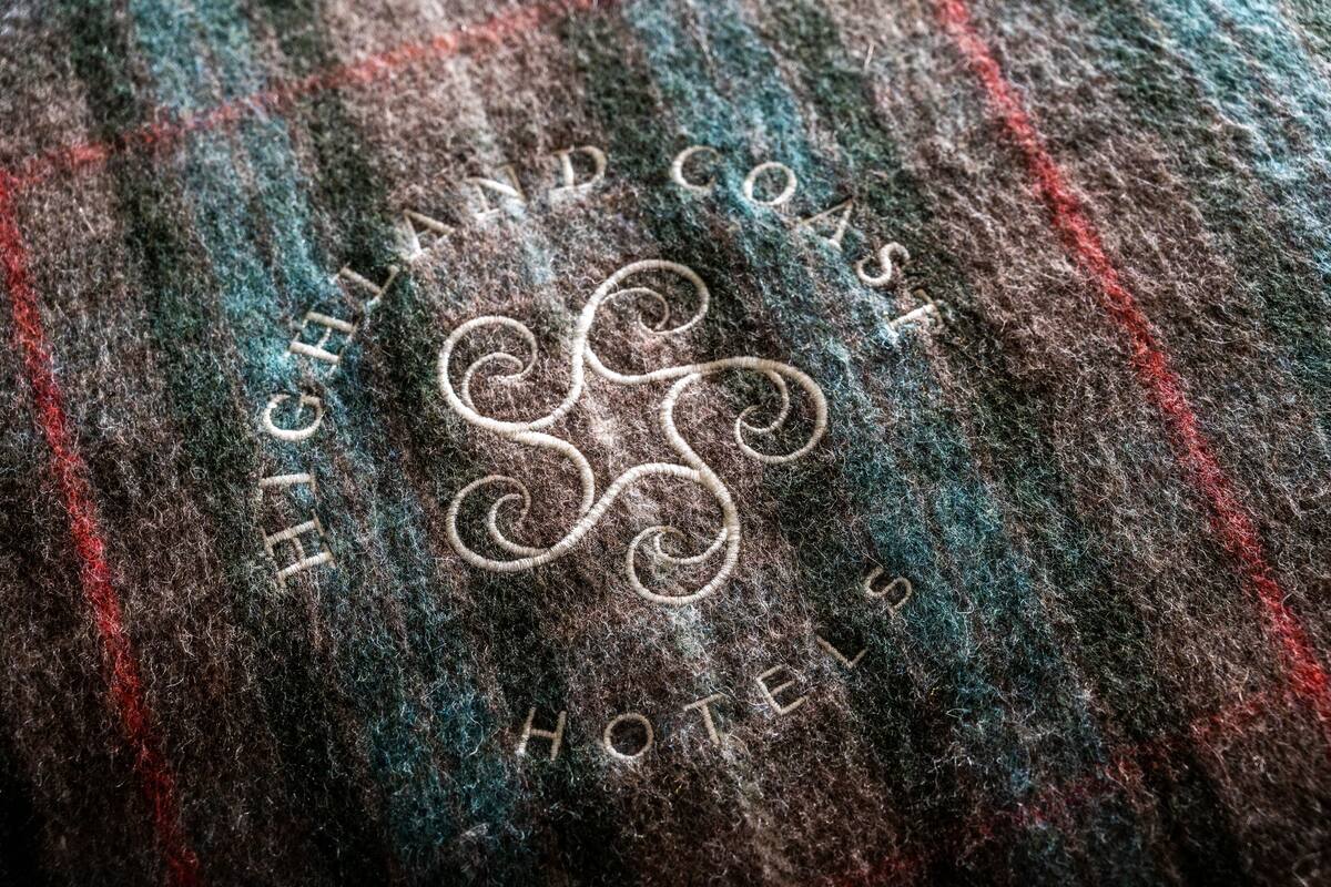 Ein gemustertes Gewebe mit eingesticktem Text: 'HIGHLAND COAST HOTELS'.